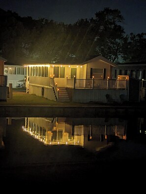 A house with a covered porch and a small deck, reflecting in a body of water.
