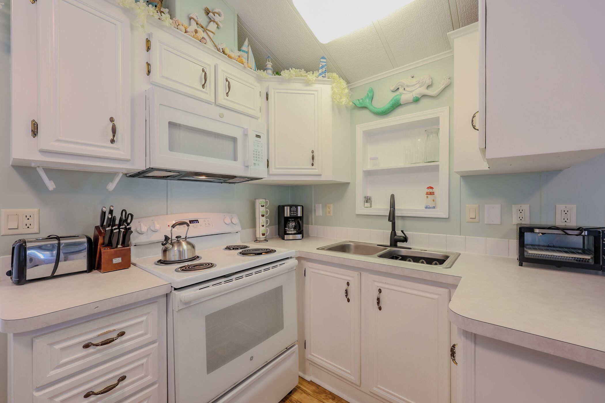 A kitchen with white cabinets, a stove, a sink, and a toaster.