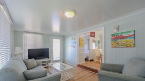 A living room with a TV, two grey sofas, a coffee table, and a door leading to another room.