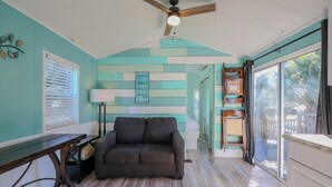 A room with teal walls, a wooden ceiling fan, a dark brown sofa, a wooden table, and a large window with blinds. - 2885 Crater Lake - Sleeps 4 (Myrtle Beach)
