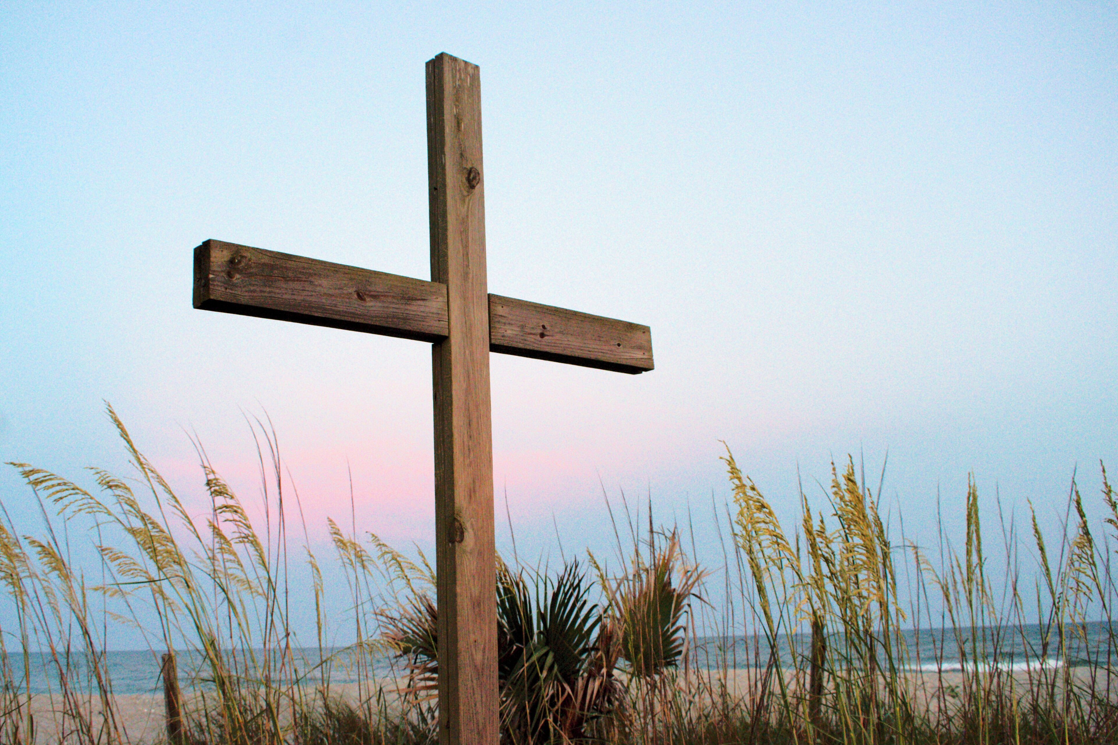 A wooden cross on a beach with ocean in the background.