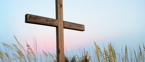 A wooden cross on a beach with ocean in the background.