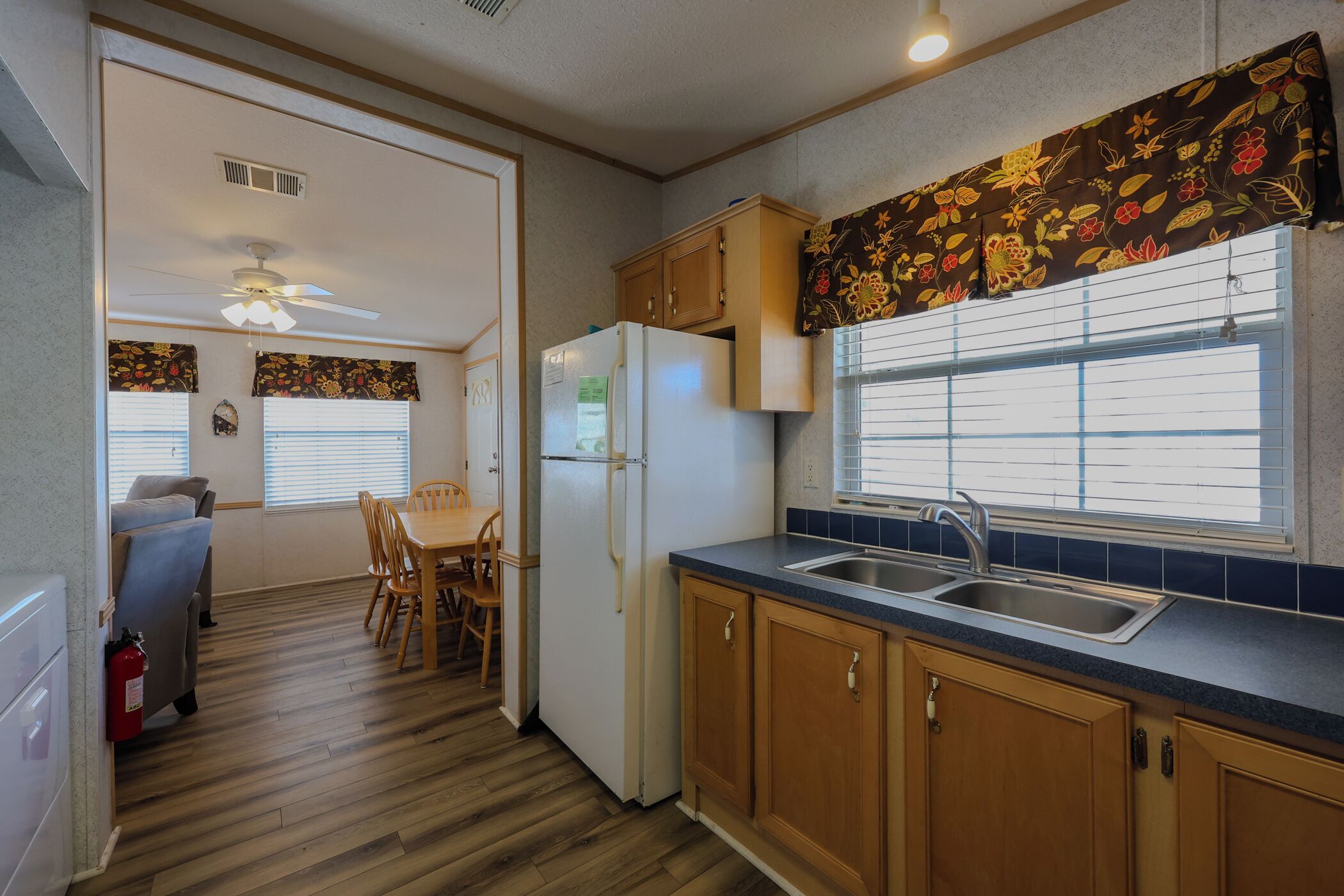 A compact kitchen with wooden cabinets, a refrigerator, and a window with blinds.