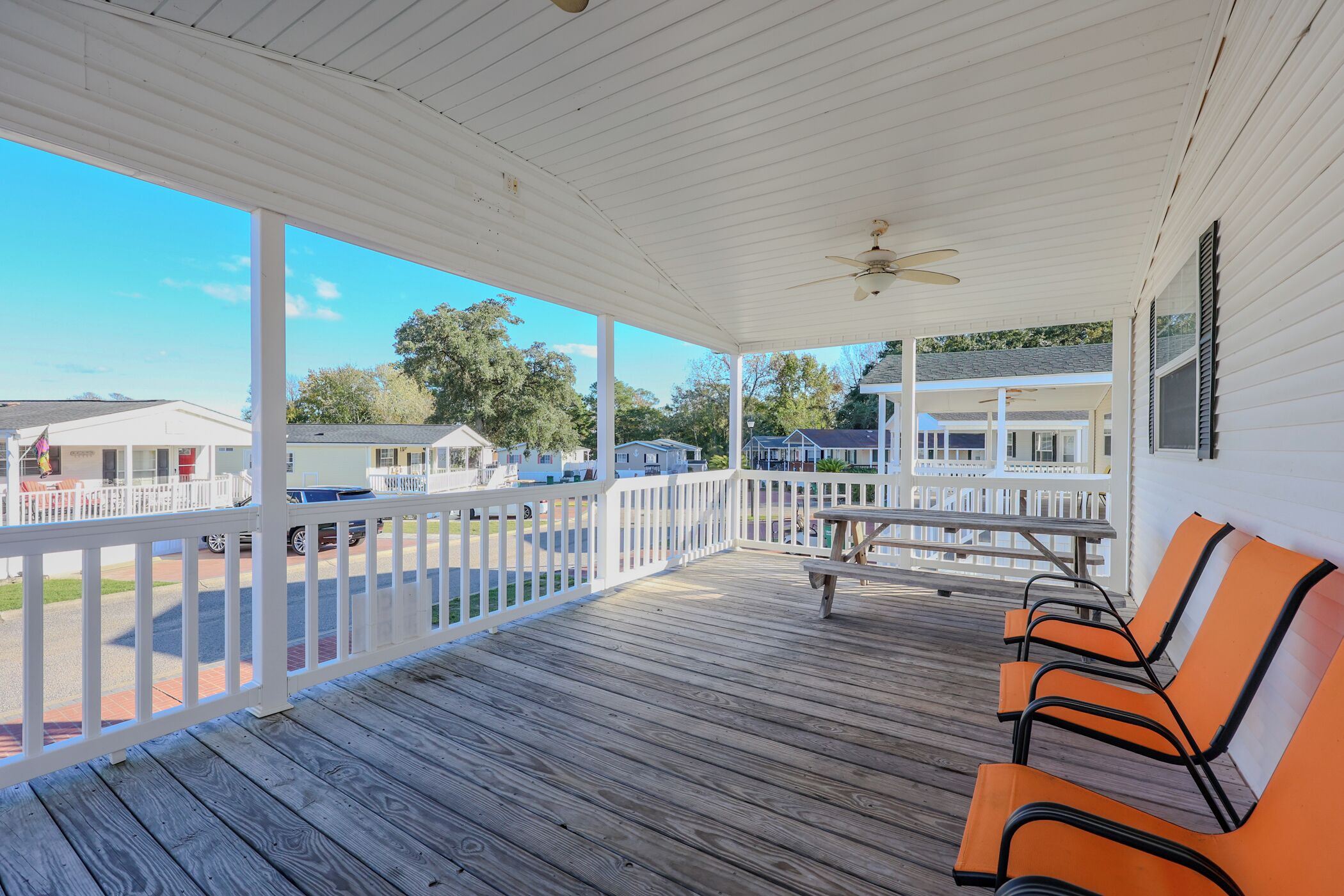 A covered outdoor area with a wooden deck, white railings, and orange chairs.