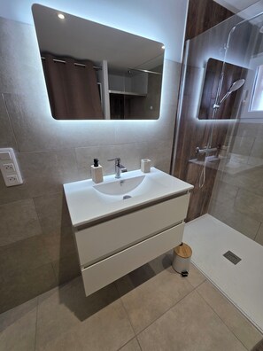 Ein modernes Badezimmer mit Waschbecken, Spiegel und einer Duschkabine.