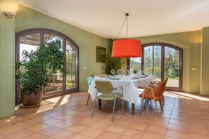 Comedor con una mesa dispuesta para cuatro personas, rodeada de sillas, una planta grande en maceta y una lámpara colgante roja.