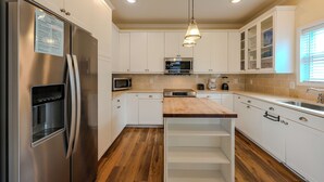 A modern kitchen with white cabinets, stainless steel appliances, a wooden countertop, and a built-in island with a sink. - 8046 Seascape- Sleeps 10 (Myrtle Beach)