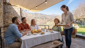 A group of people dining outdoors with a table set for breakfast, a stone wall, and a view of the countryside. - Relax Nature |8 P | BBQ | Wi-Fi | Pool | Foosball (Molló)