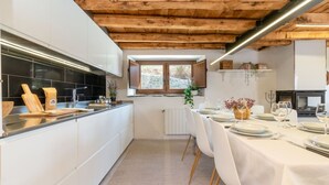 A modern kitchen with white cabinets, a wooden ceiling, and a dining area set for six with white tablecloths and chairs. - Relax Nature |8 P | BBQ | Wi-Fi | Pool | Foosball (Molló)