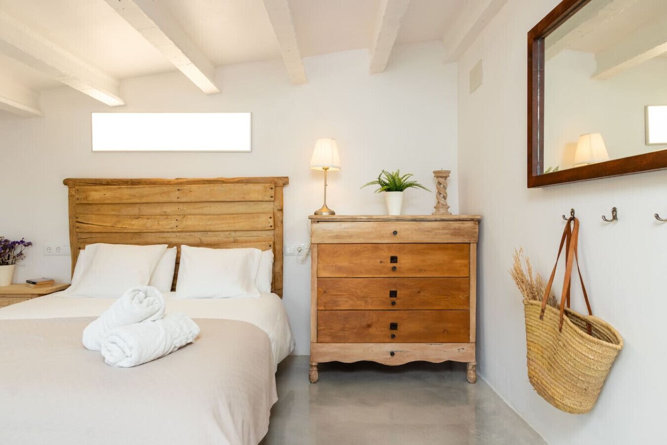 A bedroom with a wooden bed, a wooden dresser, a mirror, and a hanging basket.