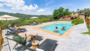 Ein Poolbereich mit Liegestühlen und Sonnenschirmen, umgeben von viel Grün und Hügeln.