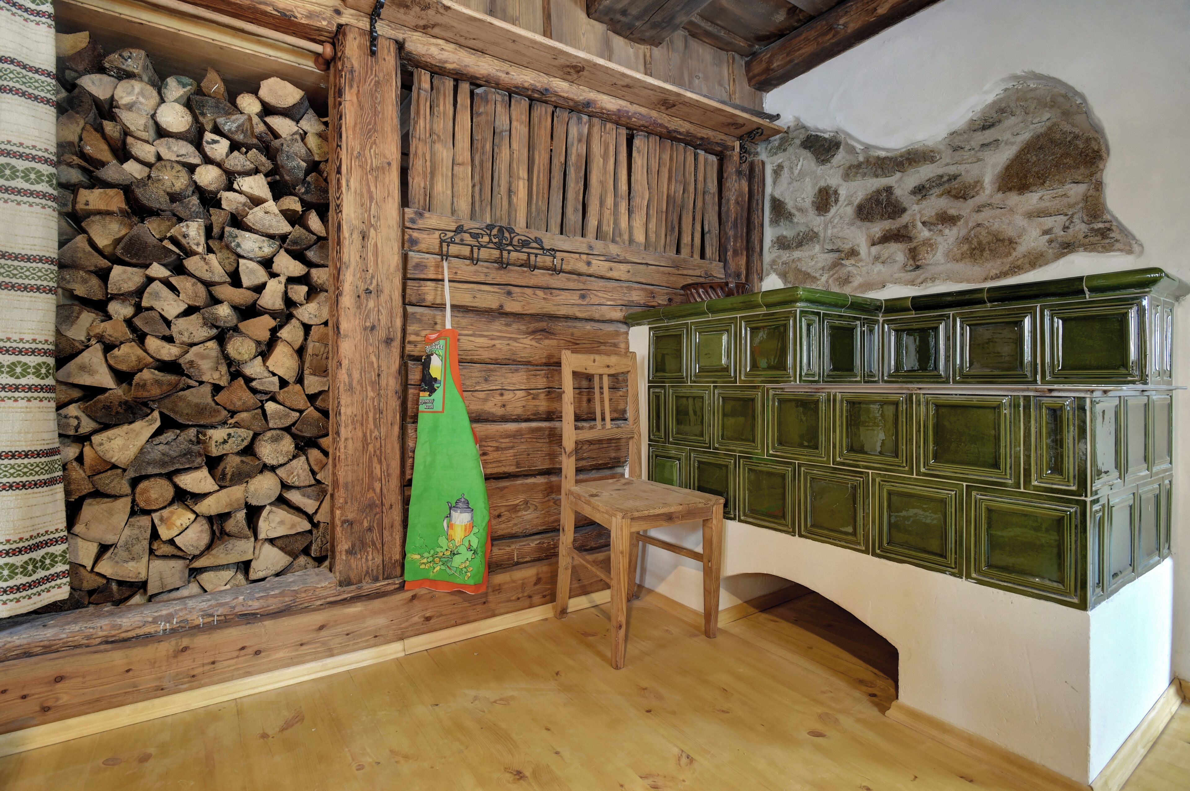 Une pièce rustique avec un mur en bois, une pile de bois de chauffage, un tissu vert, une chaise en bois et des armoires vertes.