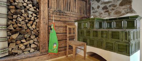 Une pièce rustique avec un mur en bois, une pile de bois de chauffage, un tissu vert, une chaise en bois et des armoires vertes.