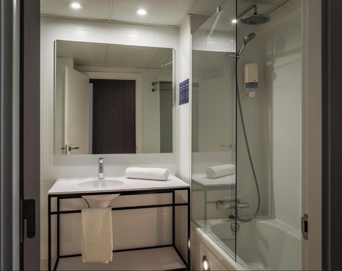 Un baño moderno con ducha envuelta en vidrio, un lavabo blanco y un espejo grande.