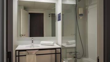 Un baño moderno con ducha envuelta en vidrio, un lavabo blanco y un espejo grande.