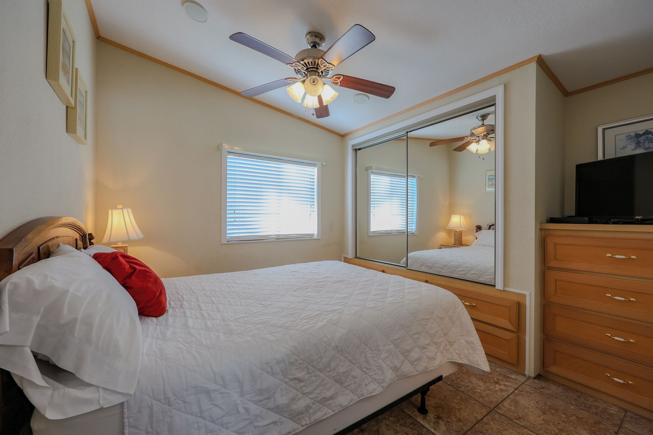 A bedroom with a bed, a ceiling fan, a dresser, a TV, and a large mirror.