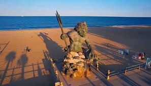 En skulptur på stranden, föreställande en stor figur som håller ett spjut, omgiven av ett staket och en utsiktsplattform.