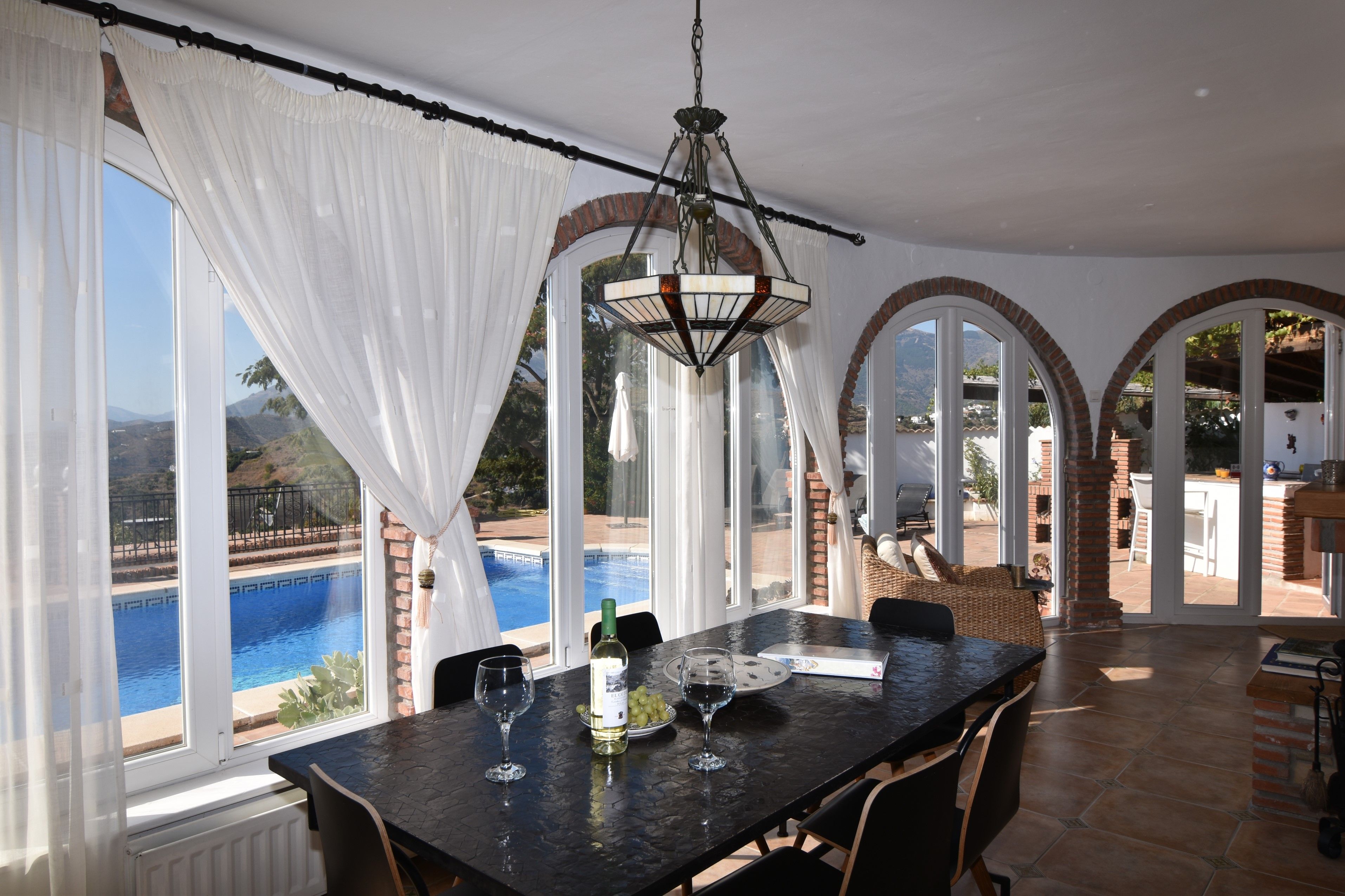 A dining area with a view of a swimming pool, large windows, and a hanging light fixture.