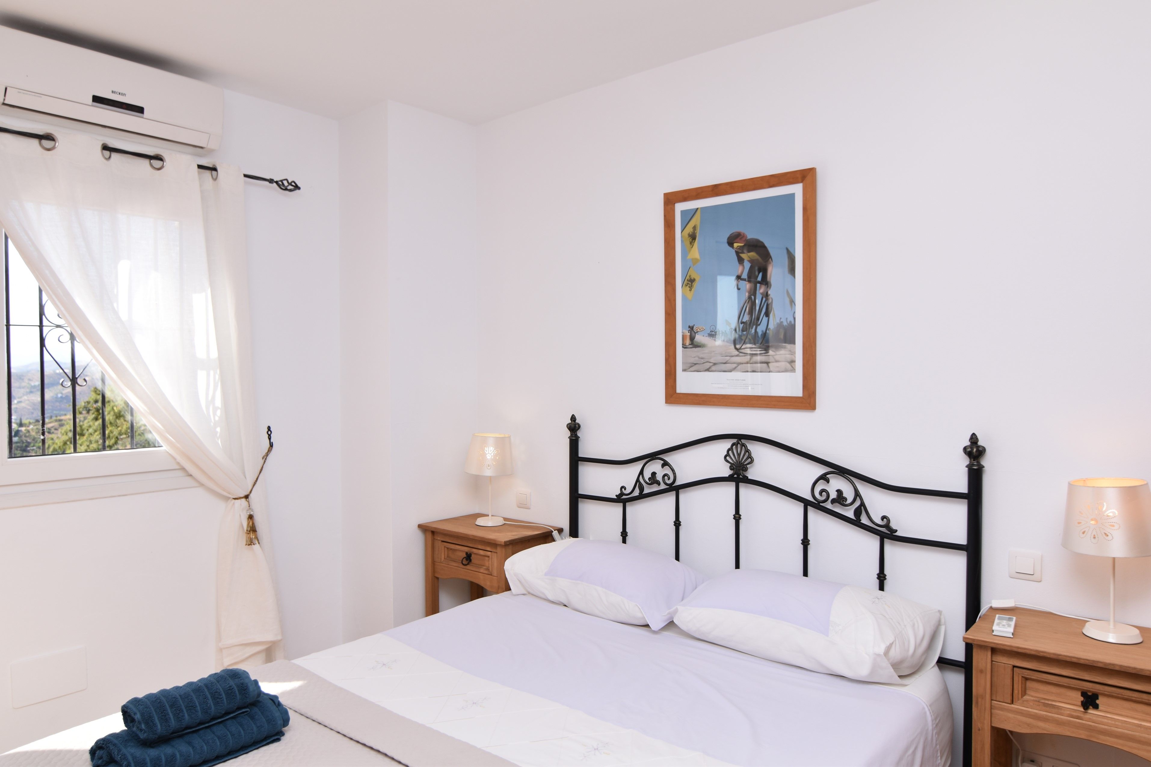 A bedroom with a bed, two bedside tables, a window with curtains, and a framed picture on the wall.
