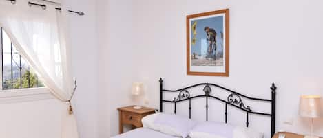 A bedroom with a bed, two bedside tables, a window with curtains, and a framed picture on the wall.