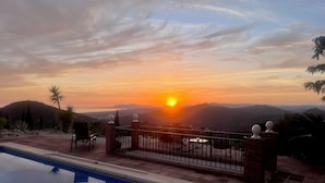Zwembad met uitzicht op een zonsondergang, een terras van baksteen en een metalen hek.