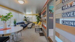 A modern living room with a dining table, sofas, and a coffee table. There are plants and a sign on the wall. - 7229 Block 3- Sleeps 2 (Myrtle Beach)