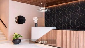 Een hal met een houten plafond, een receptiebalie, een trap en een muur met een geometrisch patroon.