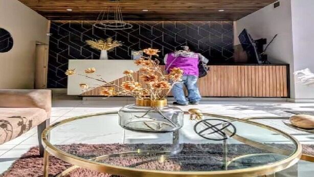 Een modern interieur met een houten plafond, een receptiebalie en een ronde glazen salontafel met decoratieve objecten.