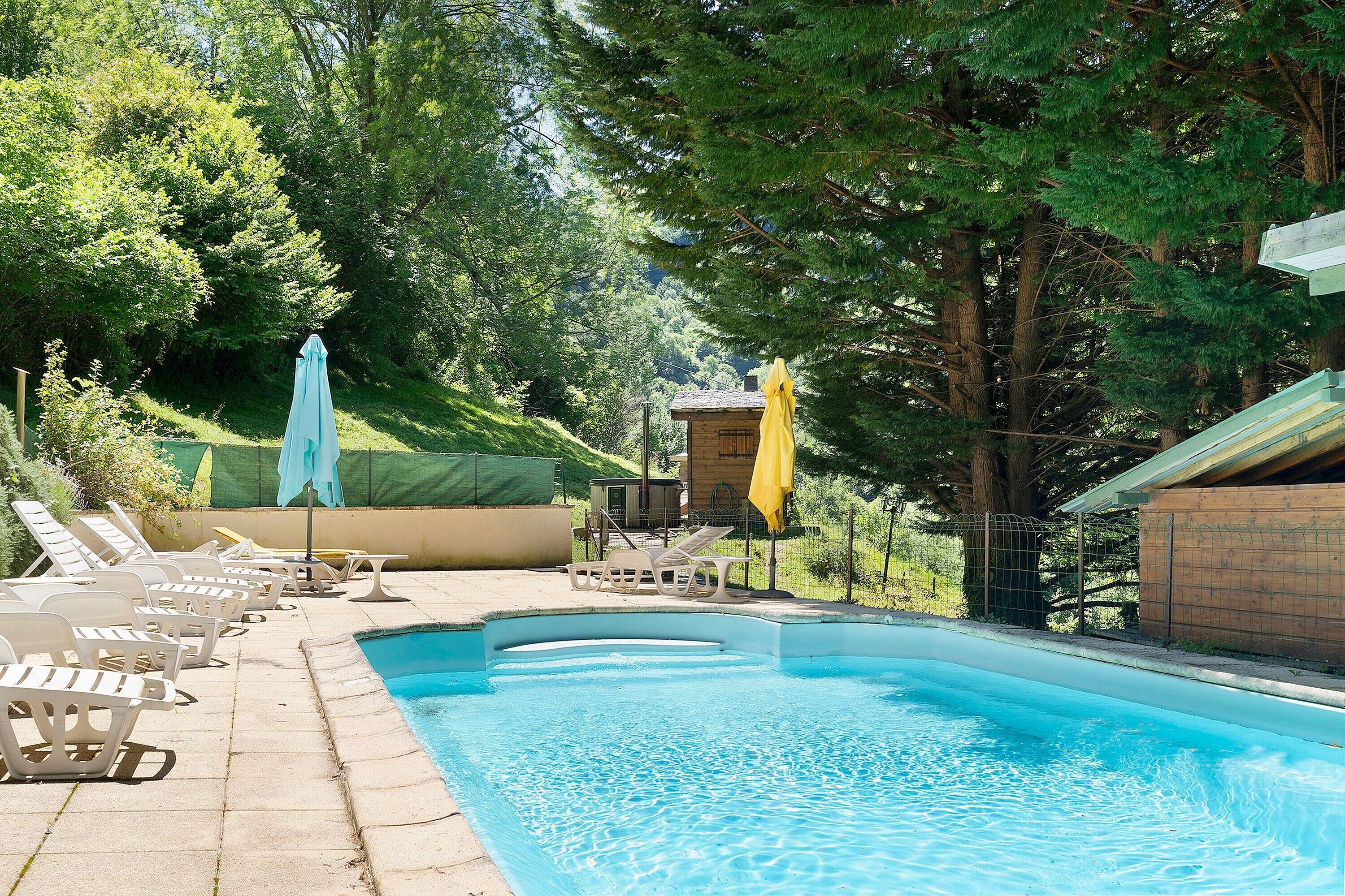 Ein Schwimmbecken mit Liegestühlen und Sonnenschirmen, umgeben von Bäumen.