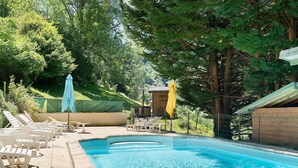 A swimming pool with lounge chairs and umbrellas, surrounded by trees. - Holiday Home 'Les Trois Maisons - Gite Jaune' with Mountain View, Shared Pool and Wi-Fi (Osse-en-Aspe)