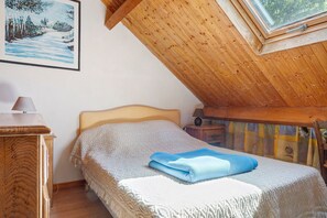 Et soveværelse med skråvægge, en seng med et mønstret dynebetræk, et sengebord med en lampe og et billede på væggen.