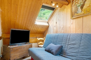 Ein Holzinterieur mit einem Fernseher auf einer Kommode, einem blau gemusterten Sofa und einem Gemälde an der Wand.