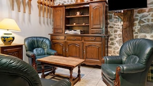 A room with a stone wall, wooden cabinets, leather chairs, a wooden table, and a television mounted on the wall. - Holiday Home 'Les Trois Maisons - Gite Vert' with Mountain View, Shared Pool and Wi-Fi (Osse-en-Aspe)