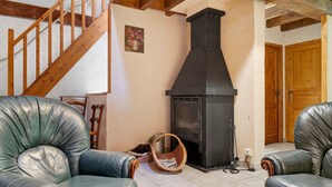 A living room with a fireplace, leather armchairs, a wooden staircase, and a wooden door. - Holiday Home 'Les Trois Maisons - Gite Vert' with Mountain View, Shared Pool and Wi-Fi (Osse-en-Aspe)