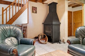 A living room with a fireplace, leather armchairs, a wooden staircase, and a wooden door. - Holiday Home 'Les Trois Maisons - Gite Vert' with Mountain View, Shared Pool and Wi-Fi (Osse-en-Aspe)