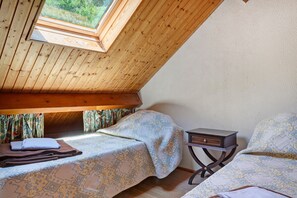 A bedroom with a sloped ceiling, a skylight, a bed with patterned bedding, a bedside table, and a window with curtains. - Holiday Home 'Les Trois Maisons - Gite Vert' with Mountain View, Shared Pool and Wi-Fi (Osse-en-Aspe)