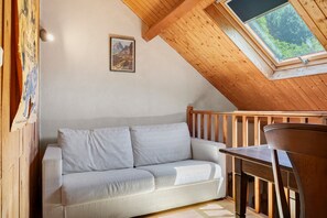 Ein Zimmer mit Holzboden, einem weißen Sofa, einem Holztisch und einem Fenster mit Blick auf Grünflächen.