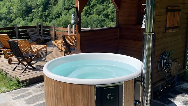 A hot tub on a wooden deck with chairs, a wooden cabin, and a forest view. - Holiday Home 'Les Trois Maisons - Gite Vert' with Mountain View, Shared Pool and Wi-Fi (Osse-en-Aspe)