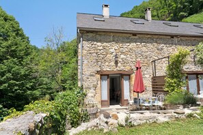A stone building with a sloped roof, a wooden door, and a red umbrella. - Holiday Home 'Les Trois Maisons - Gite Vert' with Mountain View, Shared Pool and Wi-Fi (Osse-en-Aspe)