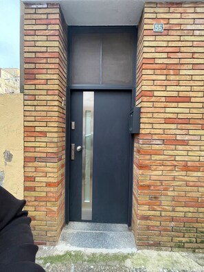 A dark-colored door with a metal handle and a glass panel, set in a brick wall with a number '55' sign above. - Ideal group- 6pax- parking van (girona)