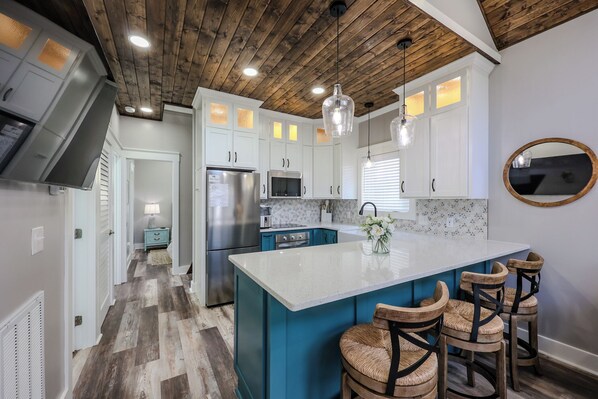 A modern kitchen with a central island, bar stools, and a wooden ceiling.
