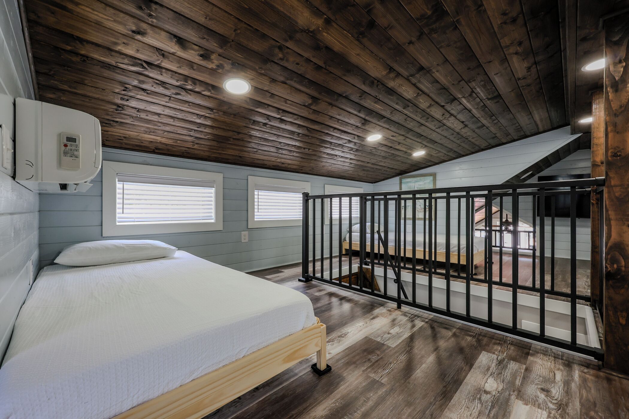 Une chambre avec un plafond en bois, un lit, une fenêtre et un balcon doté d’une balustrade.