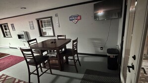 Een kleine kamer met een eettafel en stoelen, een prullenbak en een deur.