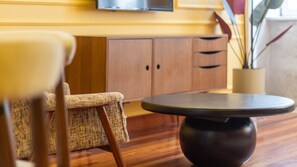 A round table with a dark base, a wicker chair, and wooden cabinets in the background. - Myo Design House: São Bento (Porto)
