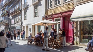 Een straat met terrasjes, gebouwen met balkons en een winkel met een rode luifel.