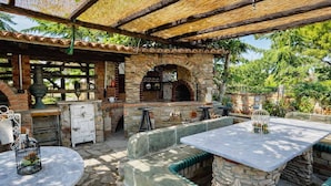 Terrassa exterior amb seients de pedra, un forn de rajola i una zona de bar rústica.