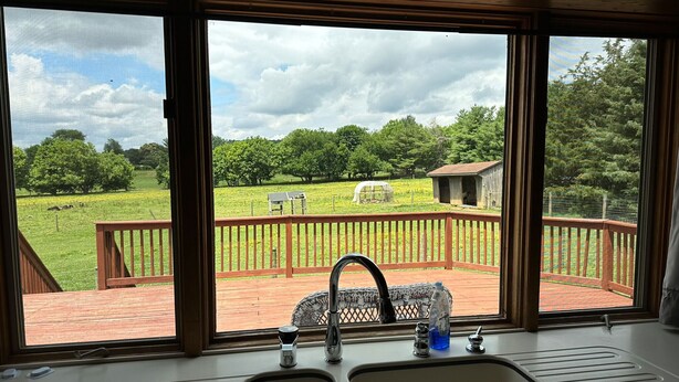 Une cuisine dotée d’une grande fenêtre donnant sur une terrasse, qui offre une vue sur un champ verdoyant et des arbres.