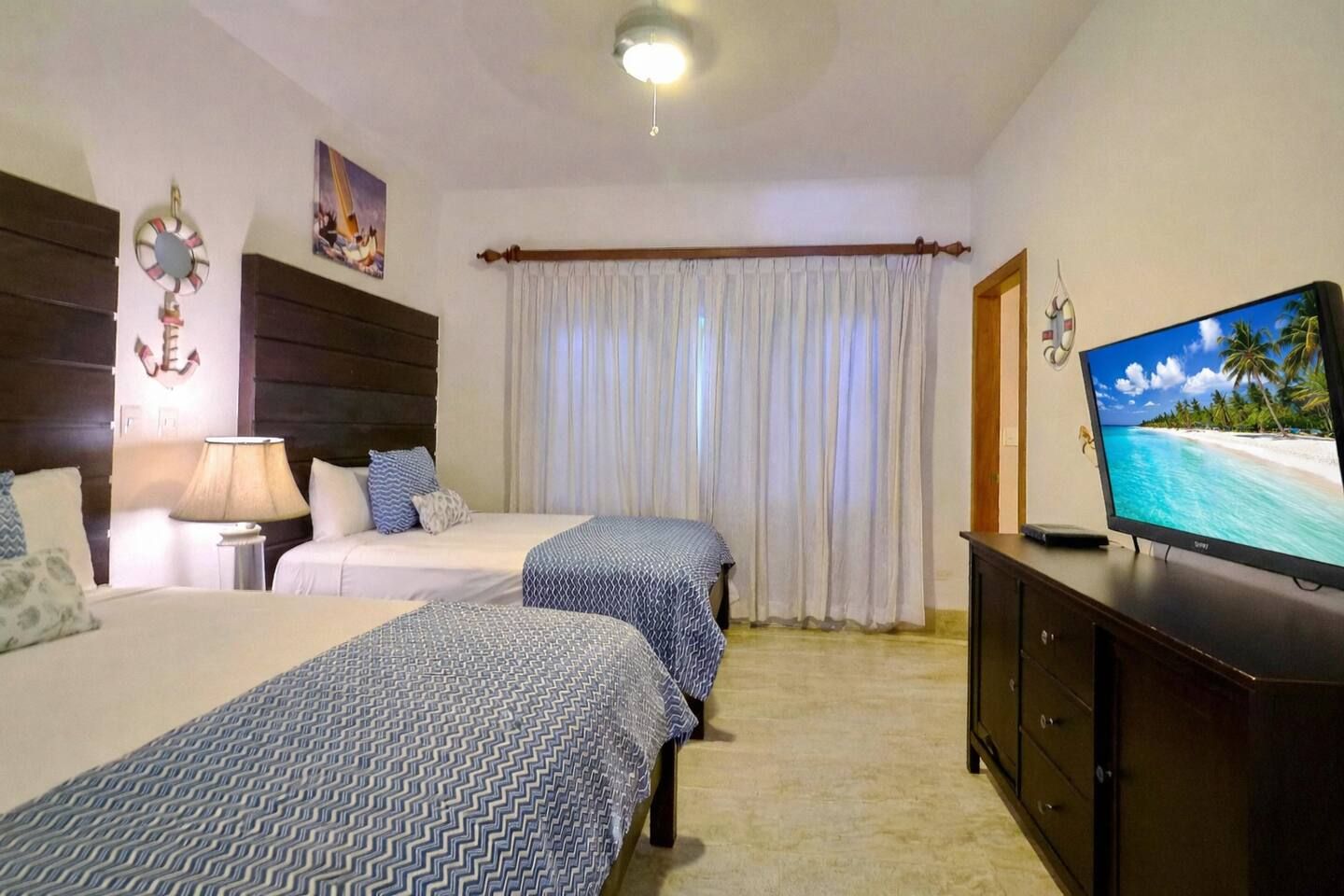 A hotel room with two beds, a television, a lamp, and a curtain.