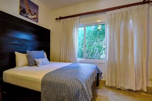 Ein Schlafzimmer mit einem Bett, einem Fenster mit Vorhängen, einem Holzkopfstück und einem Gemälde an der Wand.