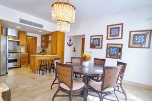 A modern kitchen with wooden cabinets, a stainless steel stove, and a dining area with wicker chairs and a central table. - ®2BR{Beach~Spot} @Terrenas+Jaccuzi+Walk~to~Beach (El Limón)